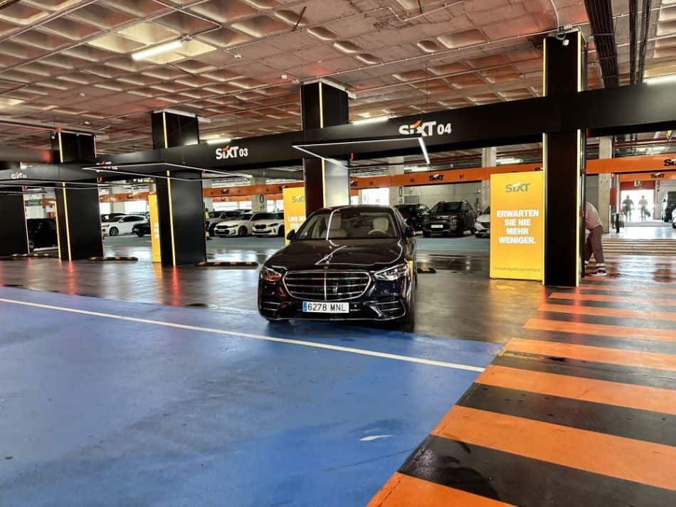 Schwarze Mercedes S-Klasse im modernen Sixt-Mietwagenbereich einer Parkgarage, umgeben von weiteren Fahrzeugen.
