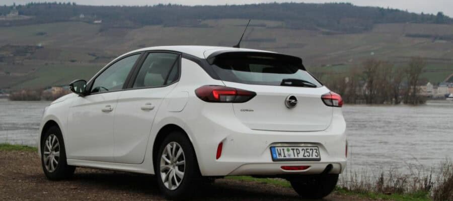 Weißer Opel Corsa der Mietwagenkategorie ECMR, geparkt am Flussufer vor Weinbergen